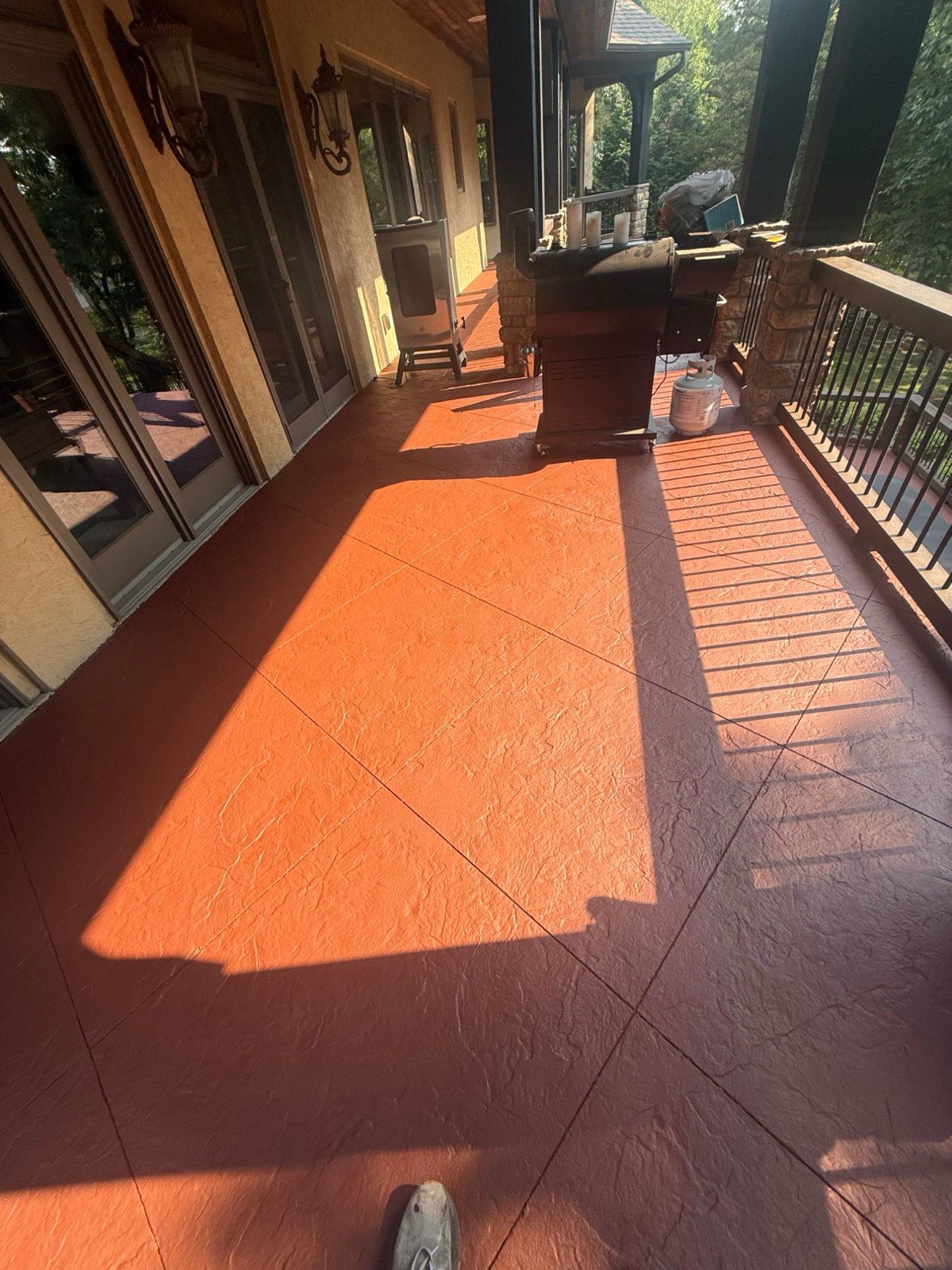 Covered balcony floor with fresh terracotta coating, stone columns, and a grill