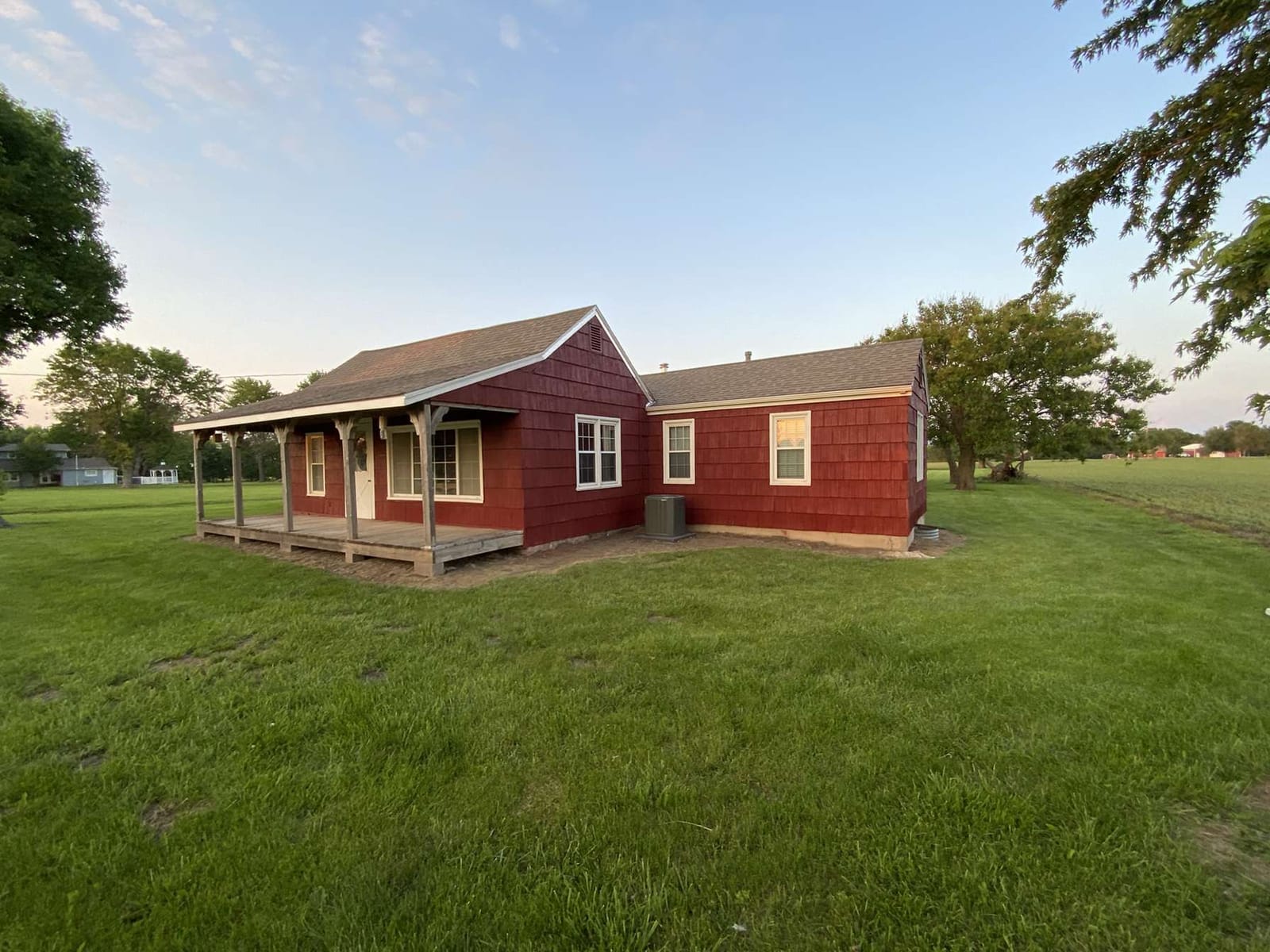 Red farmhouse with white trim and a covered porch at golden hour