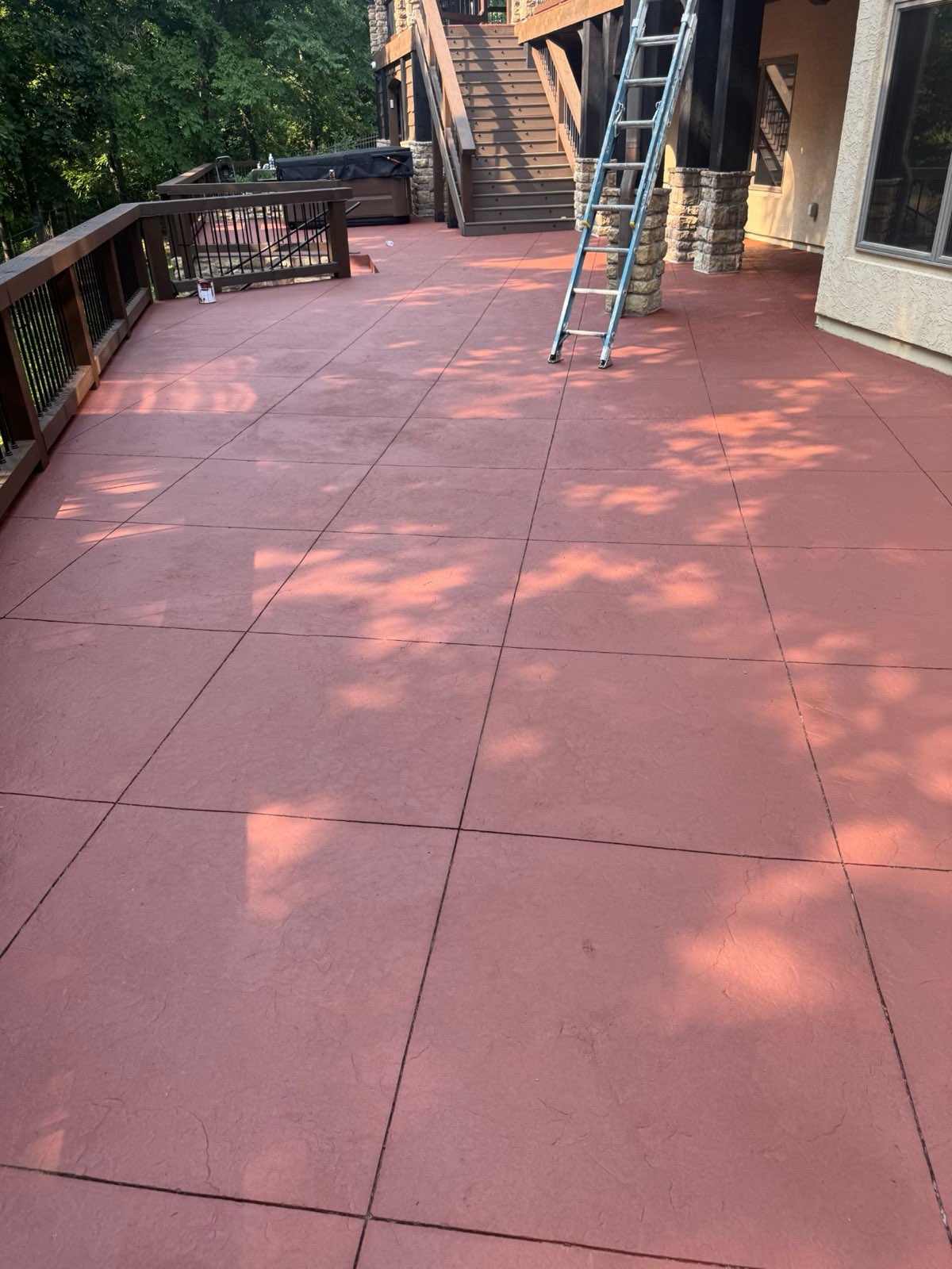 Stamped concrete patio recoated in terracotta red beside dark wood railings