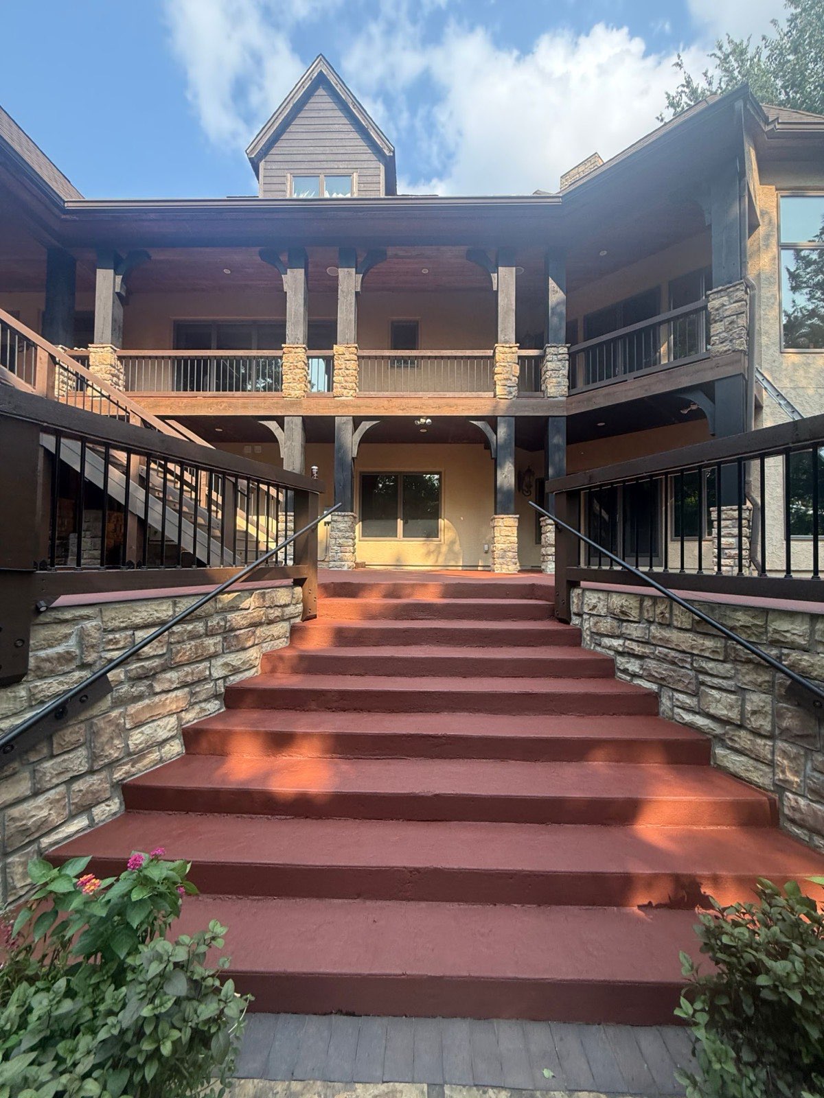 Wide outdoor staircase recoated in red leading up to a two-story timber and stone home