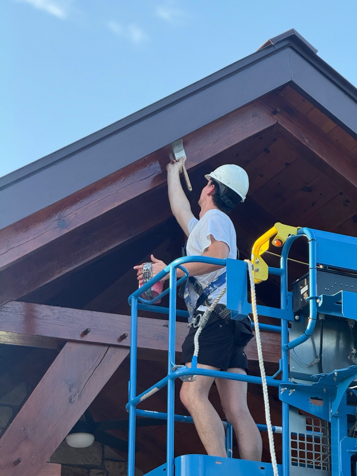 Painter in a hard hat brush-staining a timber beam under a pavilion roof